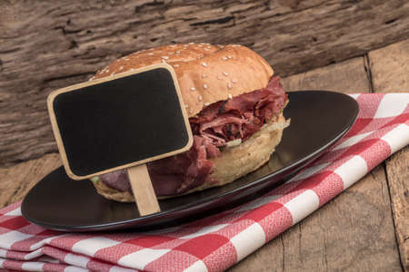 A delicious roast beef burger and an empty chalkboard on wooden tableの写真素材