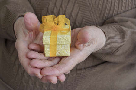 Closeup of wrinkled hands holding a yellow gift pack on palmの写真素材