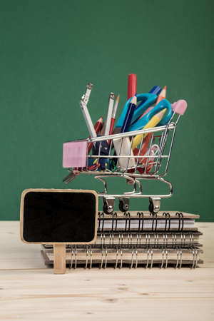 Back to school template with multiple stationery in a shopping cart and books on table over greenの写真素材