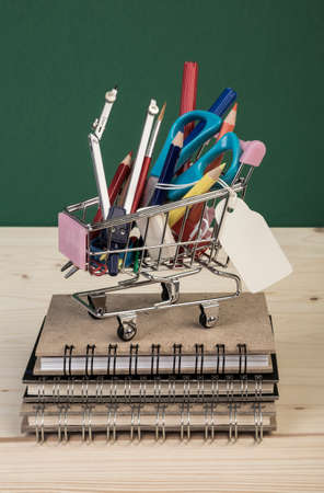 back to school template with multiple stationeries in shopping trolley on wooden table over green with name tagの写真素材
