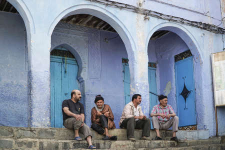Men sitting at a street of the famous blue city Chefchaouen in northern Morocco.のeditorial素材