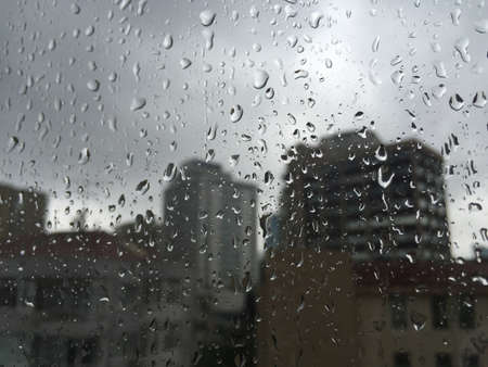 rain drops on windowpane against buildings as a backgroundの写真素材