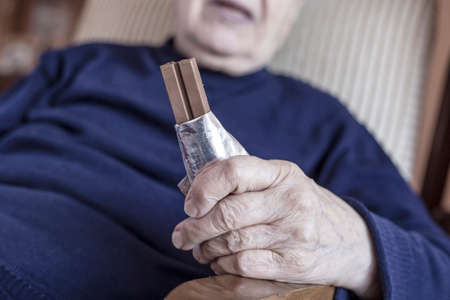 closeup wrinkled hand of a senior person holding a chocolate barの写真素材