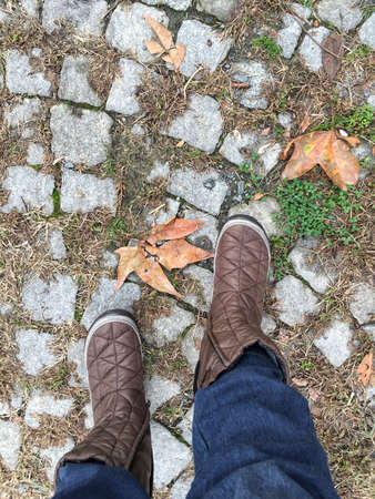 feet of a person walking on a cobblestone road in autumn