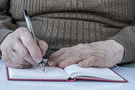 closeup wrinkled hands of a person writing on paperの写真素材