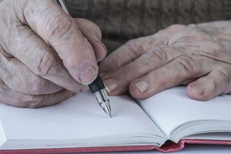 closeup wrinkled hands of a person writing on paperの写真素材