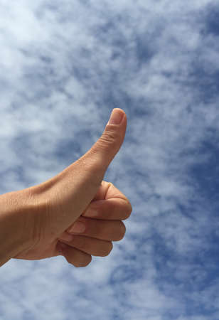 Female hand doing okay sign against blue skyの写真素材