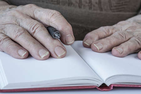 closeup wrinkled hands of a person holding a pen on paperの写真素材