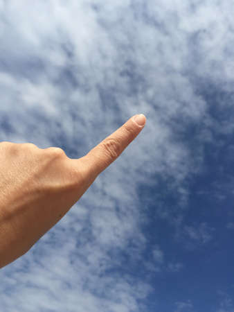 A female hand touching or pointing to something against blue skyの写真素材