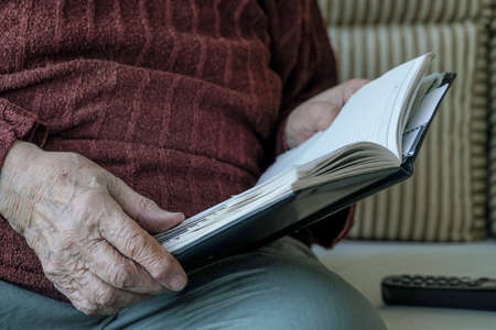 Closeup wrinkled hands of a person holding a bookの写真素材