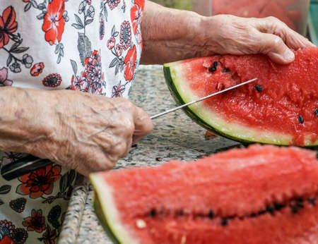 Closeup hands of a senior woman cutting watermelon in kitchenの写真素材