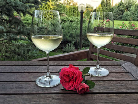 wine glasses and roses on a wooden table at garden in summerの写真素材