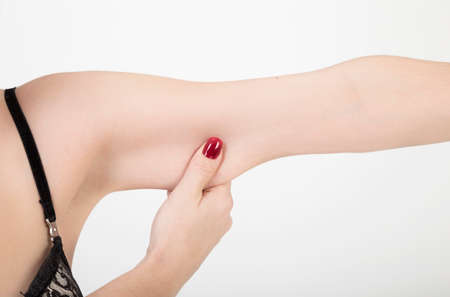 A female hand squeezing excess fat of her arm over white with copy spaceの写真素材