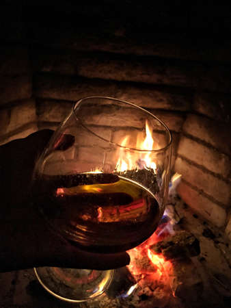 A hand holding a glass of cognac against fireplaceの写真素材