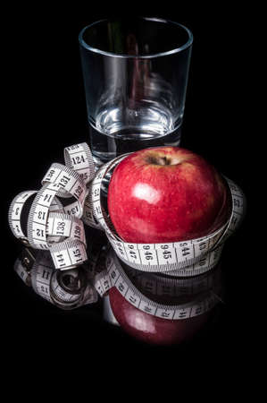 A glass of water and red apple surrounded with measurement tape on black with reflectionの写真素材