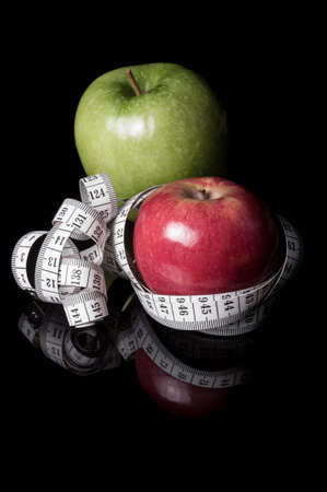 Red and green apples surrounded by measurement tapeline on black with reflection