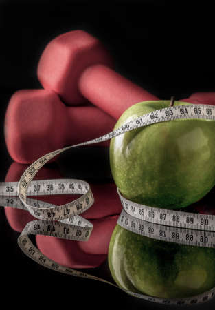 Red dumbbells and apple surrounded by measurement tape on black with reflectionの写真素材