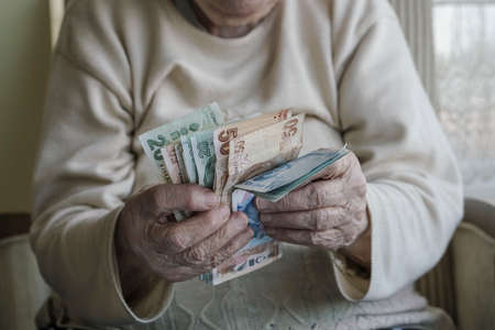 Wrinkled hands of a senior person counting turkish lira banknotesの写真素材