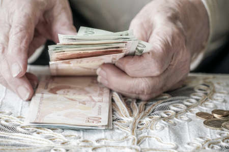 Closeup wrinkled hands of a senior woman holding Turkish Lira banknotes