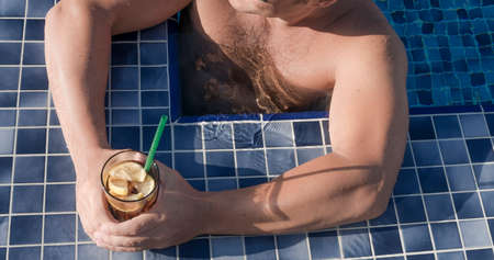 muscular arms of a man holding a drink in swimming pool