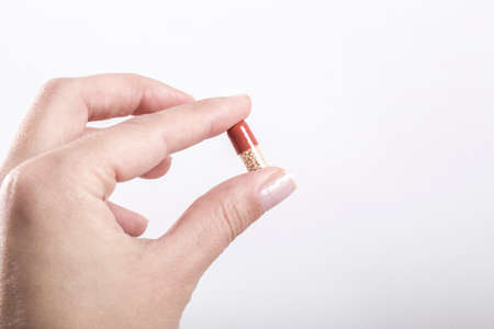 A female hand holding a pill on white