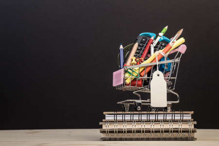 back to school template with multiple stationery in trolley with an empty label against blackの写真素材