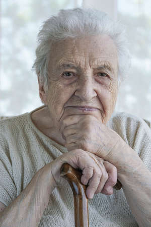 A lovely senior woman lean in on a wooden cane at homeの写真素材
