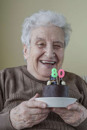 A lovely senior woman holding her birthday cake for age eightyの写真素材