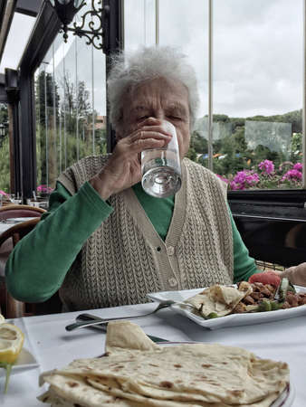 a healthy senior woman drinking a glass of water while having lunch in a cafe