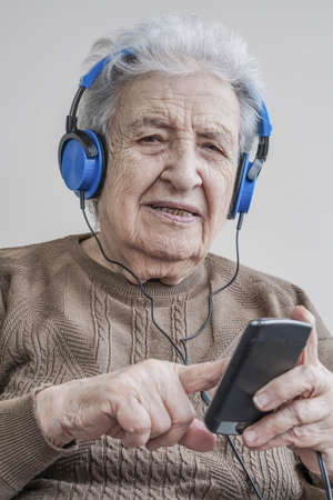 A modern senior woman listening music with blue headphones and smart phone