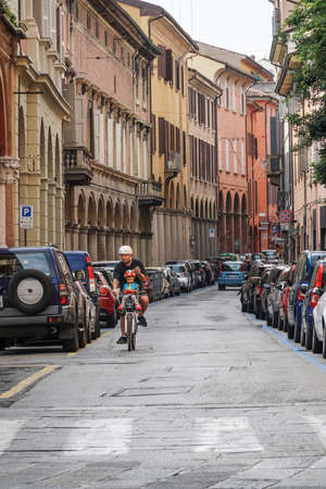 Bologna, Italy - September 10, 2016; A man riding a bicycle with his son on the road against houses and narrow street in Bologna, Italy.のeditorial素材
