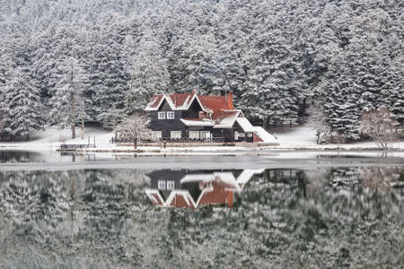 A house and pine trees under snow by lake with reflection in Turkeyのeditorial素材