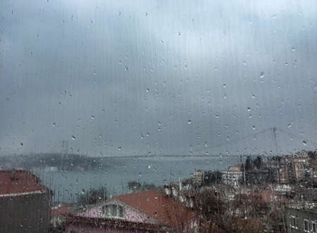 Rain drops on window pane against buildings and Bosporus Bridge in Istanbul, Turkeyのeditorial素材