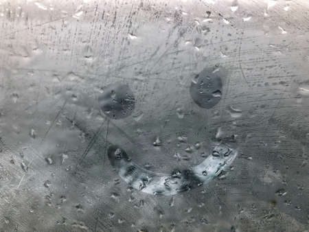 hand drawn smiley icon on the misted window pane with rain drops in a rainy day
