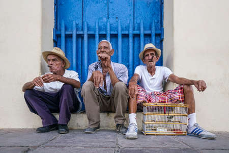 Trinidad, Cuba - May 04, 2017; Cuban men smoking cigars in front of a blue wooden door in Trinidad city of Cuba.のeditorial素材