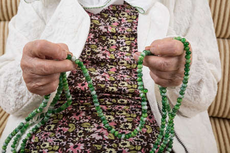 close up hands of a senior woman praying with prayer beadsの写真素材