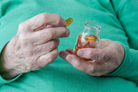 closeup wrinkled hands of a senior person holding vitamin pillsの写真素材