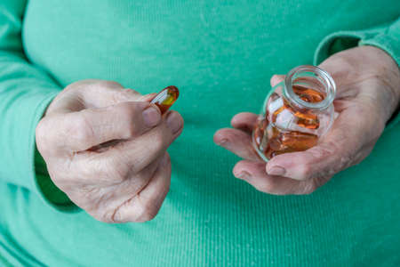 closeup wrinkled hands of a senior person holding vitamin pillsの写真素材