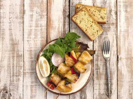 Skewed sole fish served with salad and sliced corn bread on tableの写真素材