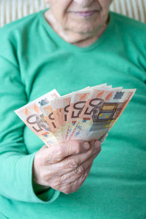 closeup wrinkled hand of a senior woman holding euro banknotesの写真素材