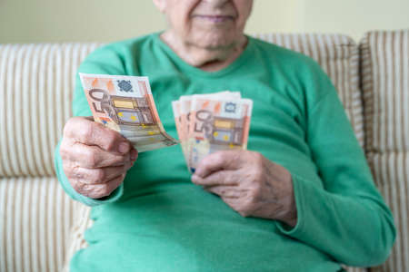 closeup wrinkled hand of a senior woman holding euro banknotes