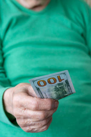 closeup wrinkled hand holding a hundred american dollar banknote