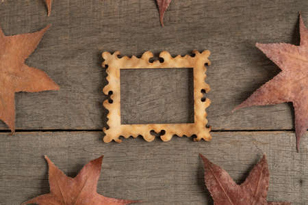 an empty picture frame on wooden background decorated with dried autumn leavesの写真素材