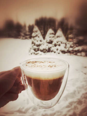 hand holding a cup of coffee against garden under snow in winterの写真素材