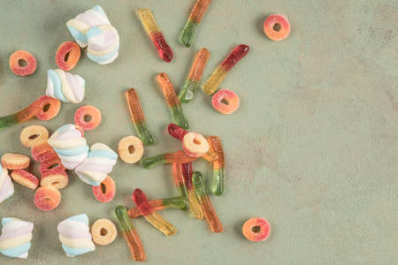 Assorted colorful jelly candies on green background with copy space. Flat lay
