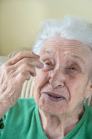 a senior woman applying eyedrops into her eyes by herself at homeの写真素材