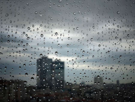 rain drops on a window pane against city view in a moody day