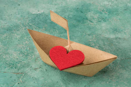 Hand crafted paper sailing boat on aquamarine background, Origami paper boat decorated with a red heartの写真素材