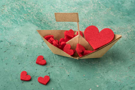 Hand crafted paper sailing boat on aquamarine background, Origami paper boat decorated with red heartsの写真素材