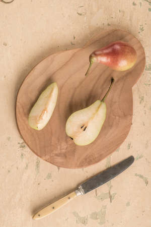halved ripe pear fruit and knife on a wooden cutting board on tableの写真素材